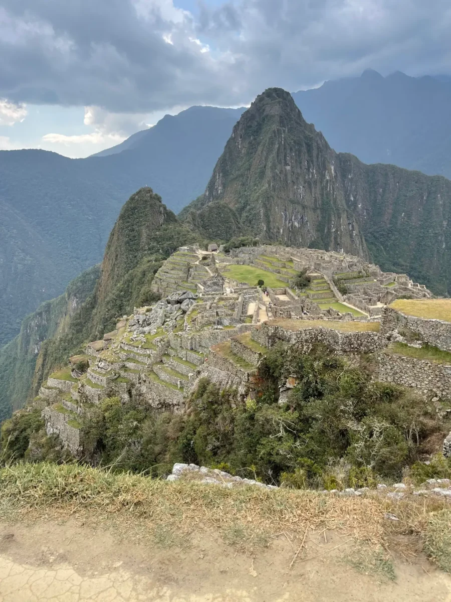 Wide shot of Machu Picchu, in the Sacred Valley of Peru, with mountain range in the far background. Photos shows the archaeological site in detail from a viewing platform.