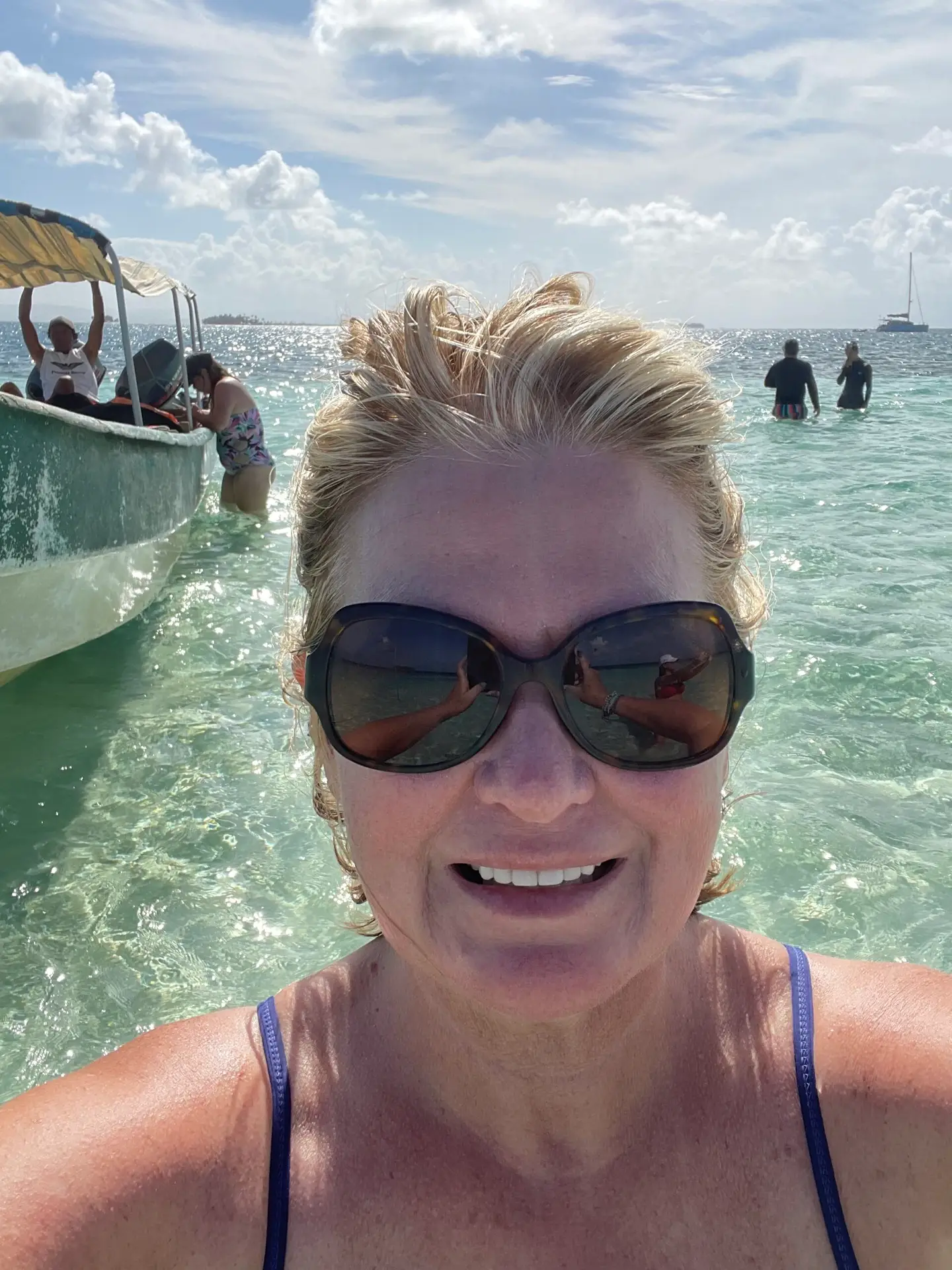 The author basking in the sun in the crystal clear waters of a natural pool in the ocean. A boat and other visitors are in the background.