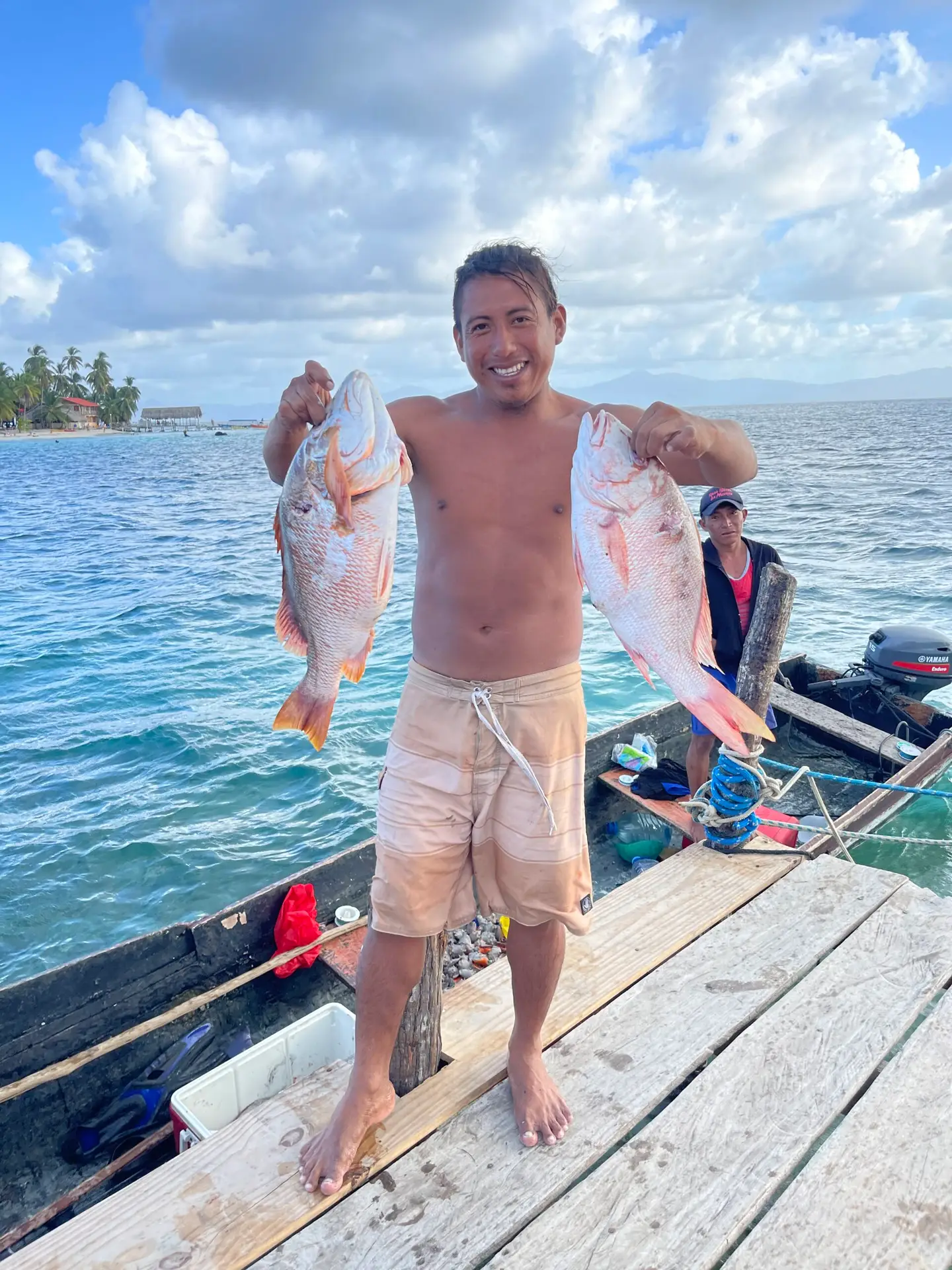 A young islander back from a day fishing, proudly holding up two large red fish.